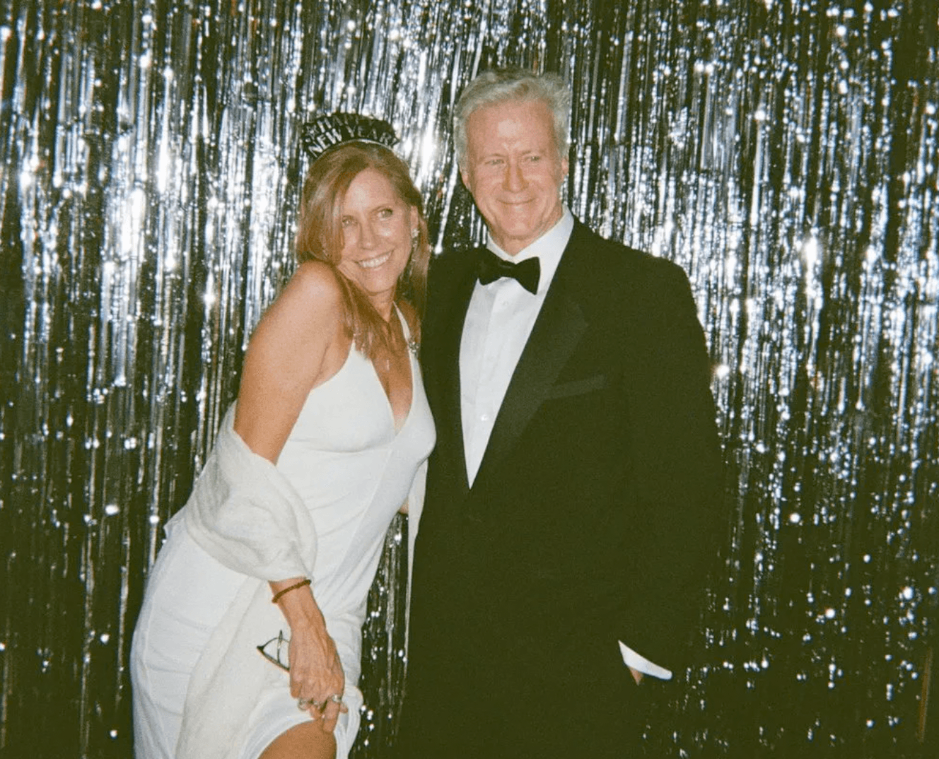 Couple in formalwear with a Happy New Year tiara in front of a silver tinsel backdrop at an NYC holiday party photo booth