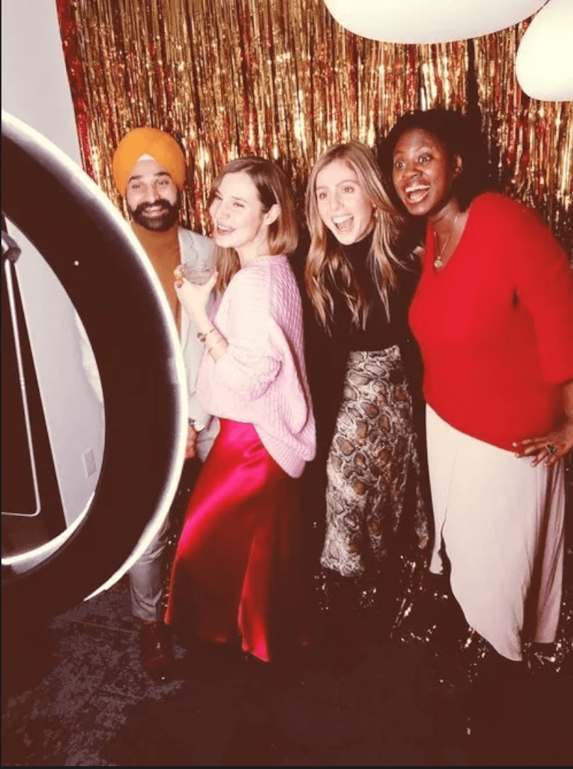 Group of four celebrating in front of a gold and red tinsel backdrop at an NYC holiday party photo booth
